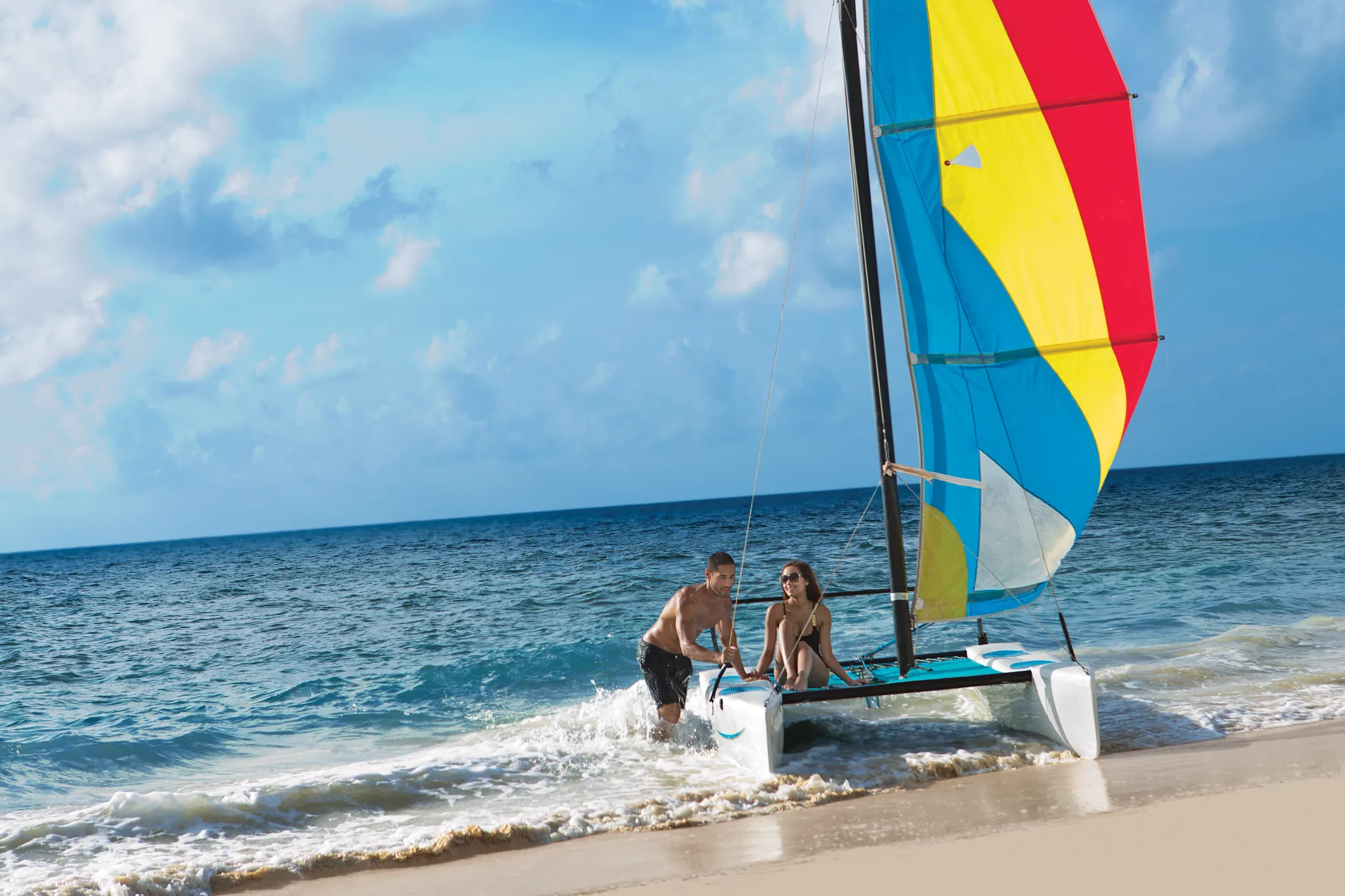 Couple launching a colorful catamaran from the beach at Dreams Sapphire Resort & Spa in Riviera Cancun.
