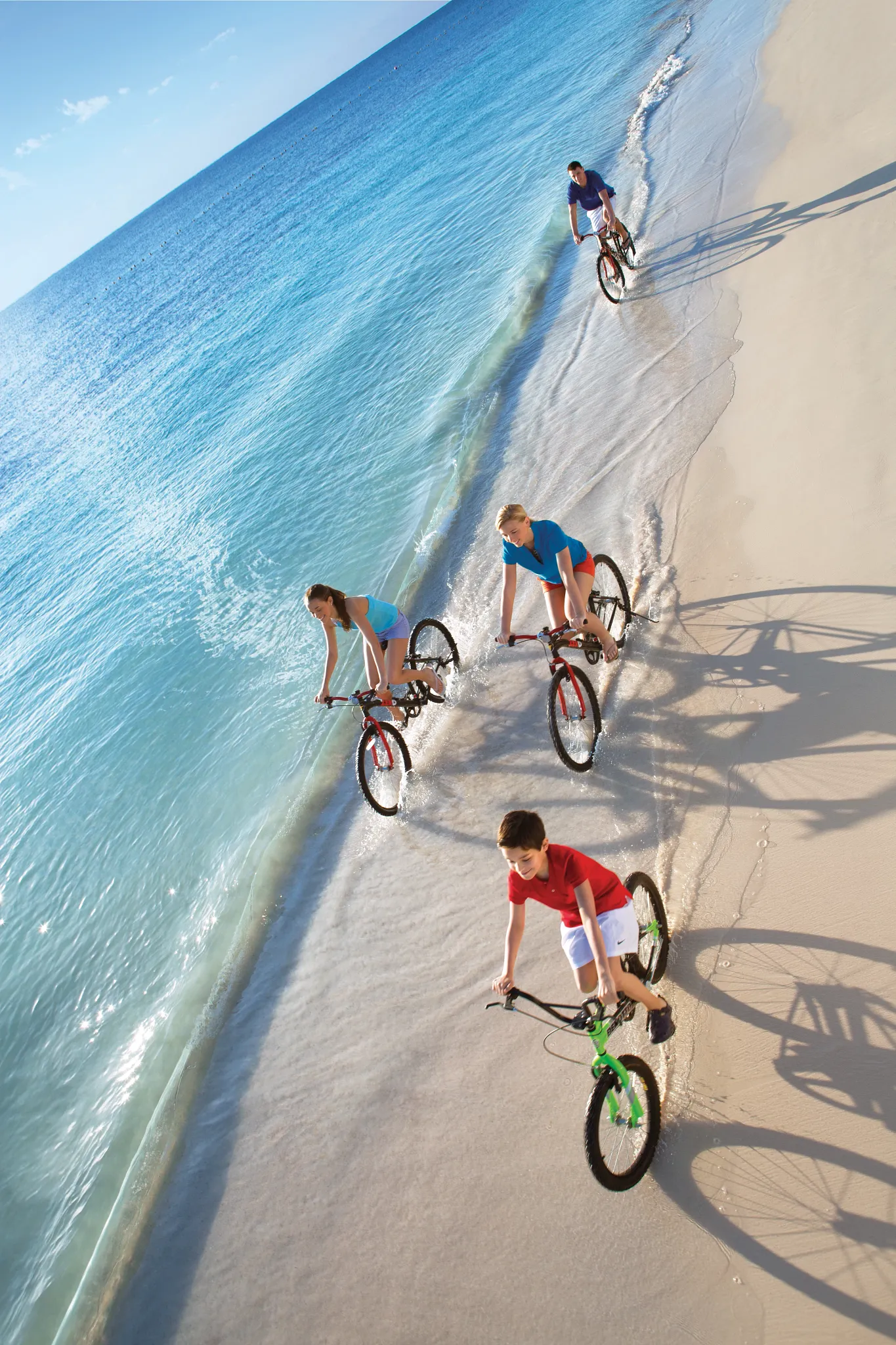 Family riding bicycles along the shoreline at Dreams Sapphire Resort & Spa, enjoying an active beach adventure in Riviera Maya.