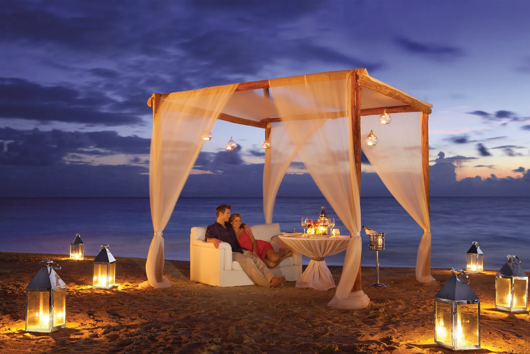 Couple enjoying a private candlelit beach dinner under a romantic cabana at Dreams Sapphire Resort & Spa in Riviera Maya.
